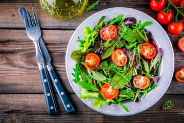 Fresh salad with mixed greens and cherry tomato on wooden background
