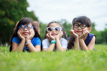 Three kid asian lying on the lawn with head in hands and looking at the camera