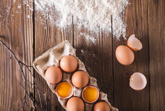 Eggs and broken eggs in the package on a wooden background. Were scattered flour on a wooden table. Eggshell. Baking  photo concept