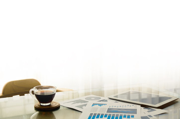 Digital tablet and cup of coffee on wooden desk. Simple workspace or coffee break in morning with paper document of finance graph/ selective focus with copy space for label text