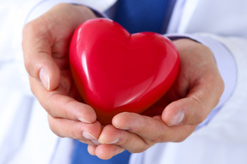 Male medicine doctor hands holding and covering red toy heart
