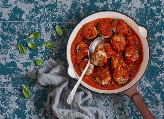 Turkey meatballs in tomato sauce in a cast iron pan on a wooden table, top view