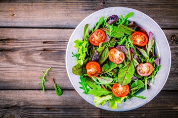 Fresh salad with mixed greens and cherry tomato on wooden background