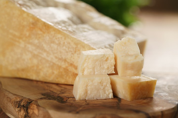 hard parmesan cheese cubes on olive cutting board, closeup photo