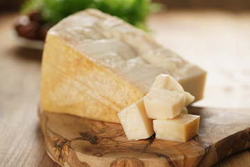 hard parmesan cheese cubes on olive cutting board, closeup photo