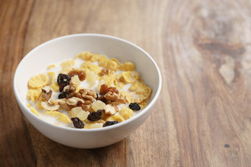 corn flakes with fruits and nuts in white bowl on wood table with copy space, healthy food