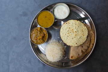 North Indian thali, a tipical meal served on stainless steel plate on blue table. Directly above.