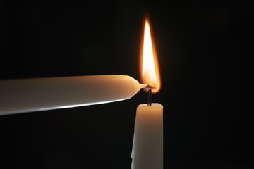 ighting tall candle with another candle in the dark, shallow focus