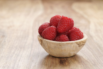 Fototapeta na wymiar ripe organic raspberries in wood bowl on old wooden table, with copy space