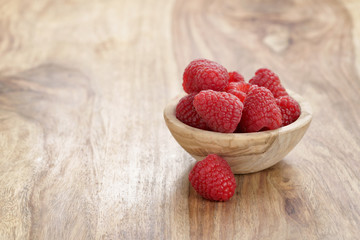 wood bowl full of ripe raspberries on old wooden table, with copy space