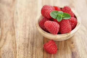 wood bowl full of ripe raspberries with mint leaves on old wooden table, with copy space