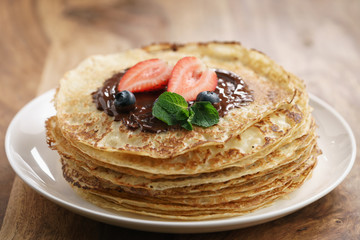 fresh blinis or crepes with melted dark chocolate and berries, shallow focus