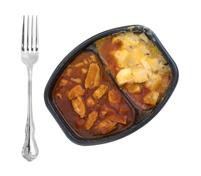 Top view of a microwaved TV dinner of chicken chunks in barbecue sauce plus potatoes and a fork to the side isolated on a white background.
