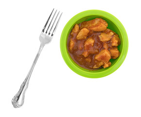 Top view of a small green bowl filled with chicken chunks in barbecue sauce plus a fork to the side isolated on a white background.