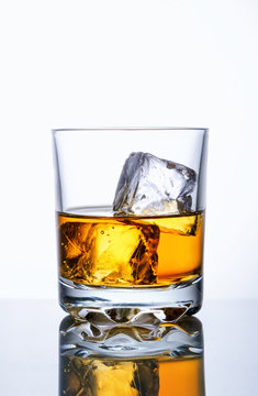 Whiskey glass with two ice cubes on white glass surface over white background
