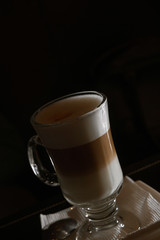 Latte coffee in transparent glass on dark background with copyspace