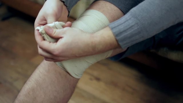 Young man unwrapping his knee injury with elastic bandage closeup