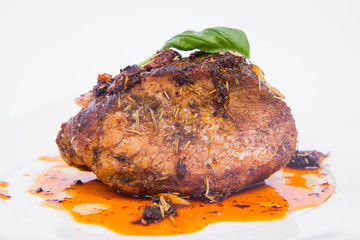 Roast pork decorated with basil on a white plate