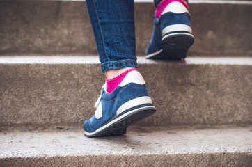 Fototapeta na wymiar Female feet in denim sneakers on the stairs