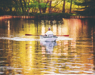an old man rowing an aluminum boat while trolling for fish in a pond