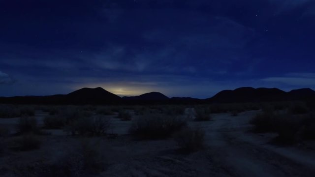 Wide angle time lapse night in Mojave desert along dirt road with clouds and planes passing in sky with city lights glowing in distance