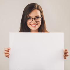Naklejka premium Young beautiful woman in glasses holding white blank board