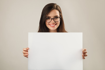 Young beautiful woman in glasses holding white blank board