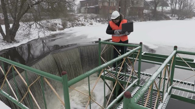 Engineer working with laptop near floodgate in winter
