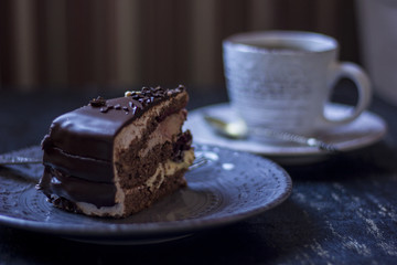 A cup of coffee together with a delicious slice of a chocolate cake on a white and dark worn out background.