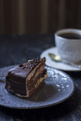 A cup of coffee together with a delicious slice of a chocolate cake on a white and dark worn out background.