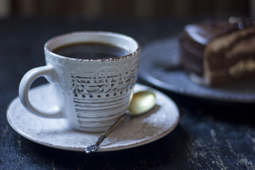 A cup of coffee together with a delicious slice of a chocolate cake on a white and dark worn out background.