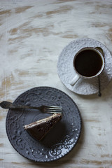 A cup of coffee together with a delicious slice of a chocolate cake on a white and dark worn out background.