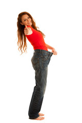 Beautiful young woman holding scale and too big trousers as she