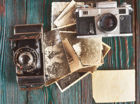 Three generations of a photo cameras and old photos on memory. Ancient authentic wooden background