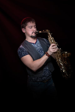 Young bearded saxophonist plays the saxophone with his eyes closed, on a black background