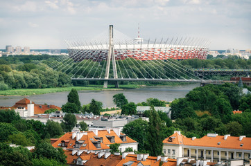 Cityscape of Warsaw. Old architecture with red roofs on the foreground, Holy Cross Bridge over the...