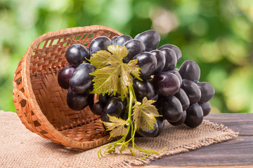 Blue grapes in a wicker basket on wooden table with  blurred background