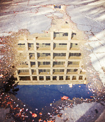 a city building reflected in the puddle of water toned with a vi