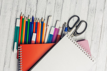 colored pencils, markers and scissors under a red notebook