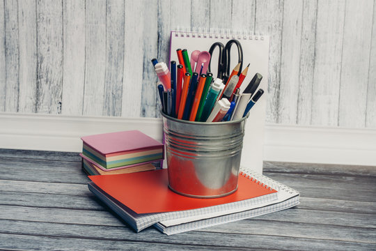 pen pencils in an iron stand, an orange notebook on a table and multicolored sheets of paper