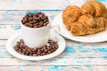 full cup of coffee beans with croissants on the old wooden backg
