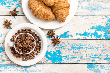Cup of coffee beans with croissants and star anise on the blue o