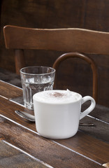 Cappuccino cup and water glass are on  the wooden table