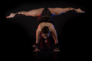 woman athlete gymnast in the form of an elf performs acrobatics on a black background in the scenic...