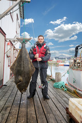 Fisherman on the pier with a big fish. halibut. - obrazy, fototapety, plakaty