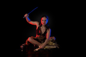 woman athlete in the Amazon costume with fur and skins posing on a black background in the scenic...