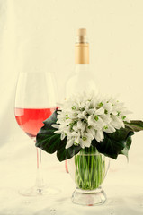 Snowdrop bouquet, white spring flowers and pink wine on light background. Copy space