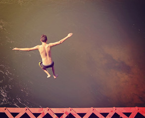 Obraz na płótnie Canvas a boy jumping of an old train trestle bridge into a river done with a retro instagram filter