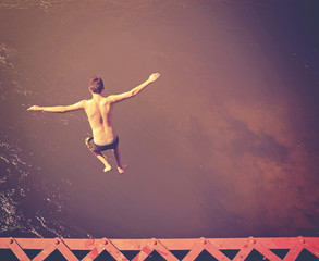 Fototapeta na wymiar a boy jumping of an old train trestle bridge into a river done w