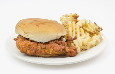 Chicken sandwich with bun and waffle fried on white plate.